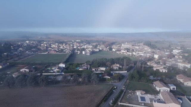 Aerial sidestep of a french village through thick morning fog at Sunris