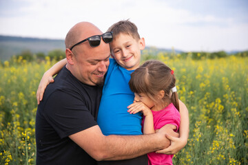 Brother and sister with their father having fun in rapeseed field. Love, friendship, and care concept.