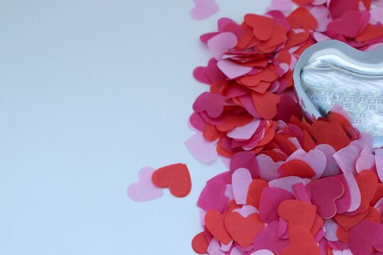 A mirrored metal heart on a white background surrounded by red, pink, and purple paper hearts &mdash; a romantic composition.