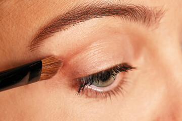 Naklejka premium Woman applying cosmetic eyeshadow to her eye using a brush
