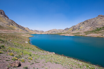 Fototapeta premium A lake in the mountains, natural scenery, green meadows, snow-capped mountains, blue sky, winter season. Lake views in bloom in spring. Hakkari Cilo Sat Lakes. A lake view in the mountains. 