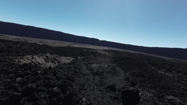 Aerial view of volcanic rock formations under a clear blue sky, creating a stark contrast of textures and tones, Saint Benoit, Reunion.