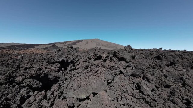 Aerial view of a stark volcanic landscape under a clear blue sky, showcasing the rugged textures and dark tones, Saint Benoit, Reunion.