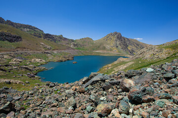 A lake in the mountains, natural scenery, green meadows, snow-capped mountains, blue sky, winter season. Lake views in bloom in spring. Hakkari Cilo Sat Lakes. A lake view in the mountains. 