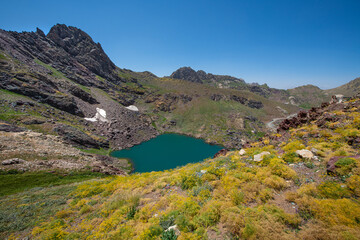 A lake in the mountains, natural scenery, green meadows, snow-capped mountains, blue sky, winter season. Lake views in bloom in spring. Hakkari Cilo Sat Lakes. A lake view in the mountains. 