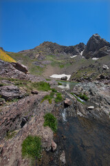 A lake in the mountains, natural scenery, green meadows, snow-capped mountains, blue sky, winter season. Lake views in bloom in spring. Hakkari Cilo Sat Lakes. A lake view in the mountains. 