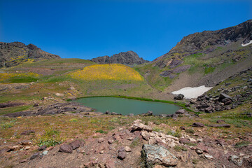 A lake in the mountains, natural scenery, green meadows, snow-capped mountains, blue sky, winter season. Lake views in bloom in spring. Hakkari Cilo Sat Lakes. A lake view in the mountains. 