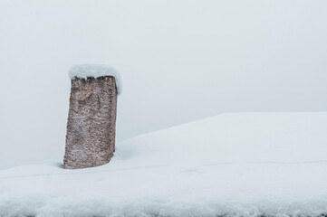 Solitary stone chimney on snow-covered roof in dense fog