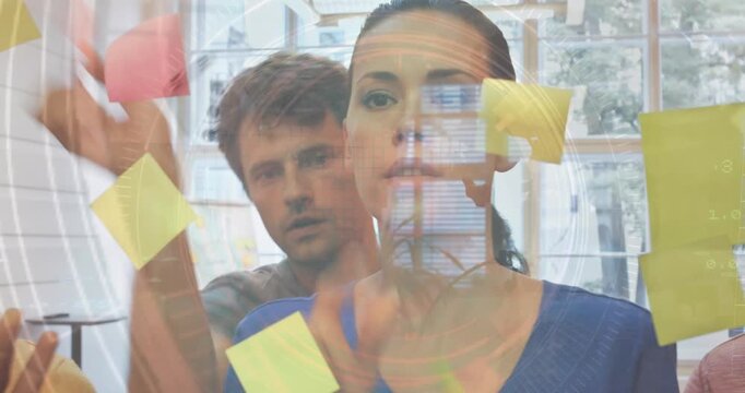 Data processing over caucasian male and female office colleagues sticking memo notes on glass board