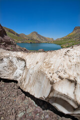 A lake in the mountains, natural scenery, green meadows, snow-capped mountains, blue sky, winter season. Lake views in bloom in spring. Hakkari Cilo Sat Lakes. A lake view in the mountains. 