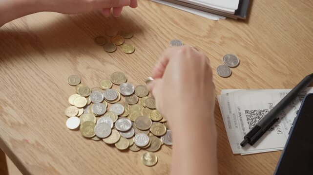 Woman hands sorting and organizing pile of metal coins cash at home with sound. Person planning household budget, dividing savings or calculating expenses with paper receipts on desk.