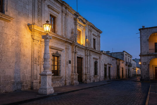 Fotograf&iacute;a nocturna de una calle empedrada en el centro hist&oacute;rico de Arequipa, destacando una casona colonial de sillar blanco con fachada barroca mestiza iluminada por un farol de hierro ornamental