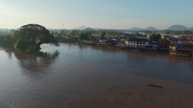 Small boat traveling across a wide river near Don Det, Laos, with riverside houses, trees, and calm evening light.