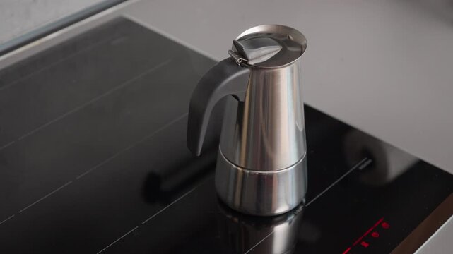 Moka pot geyser coffee maker prepares espresso on induction stovetop. Sound of boiling water and hiss of steam. Steel kitchen appliance heating drink in minimalist home kitchen environment.