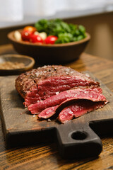Freshly sliced meat served on a wooden cutting board with vegetables in the background
