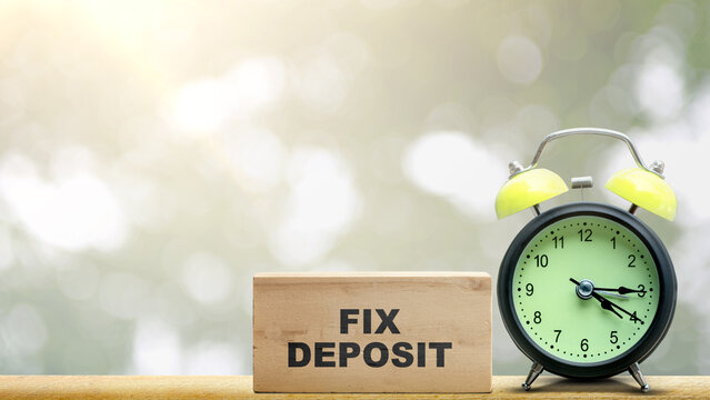 A wooden block with FIX DEPOSIT text next to an alarm clock on a wooden table, symbolizing time-bound financial investments and savings planning with copy space