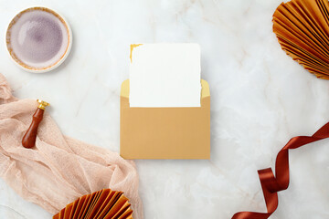 Wedding invitation mockup with a blank card in a golden envelope on a marble background.