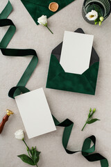 Top view blank paper cards wedding invitations, flowers, green envelopes, ribbon on stone table.