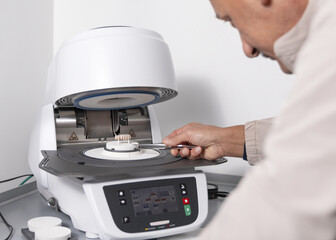 Orthodont men puts tooth implants into dental ceramic oven for baking enamel. Dental prosthetics