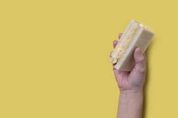 Hand holding Tamago Sando sandwich on yellow background. Copy space