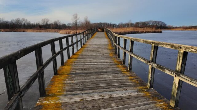 Wooden boardwalk leading over frozen marsh water at Crosswinds Marsh, Michigan in winter, USA