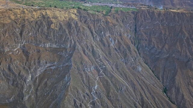 A distant drone shot follows the descending trail before reversing to reveal the Colca Canyon rim, contrasting lush farmland in Cabanaconde with the steep, barren drop into the canyon.
