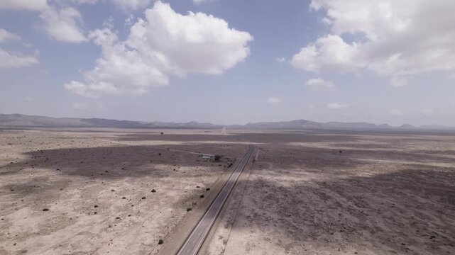 Aerial push in over a desolate desert highway, cumulus clouds cast shadows over the vast landscape