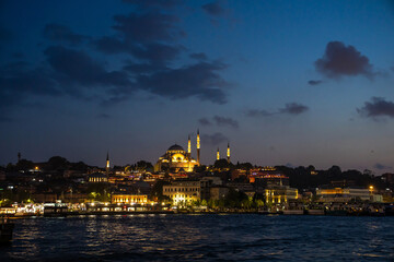 Obraz premium Sultanahmet district in twilight. Illuminated Eminonu pier, Suleymanie mosque and Egyptian market, view from the cruise boat at Bosphorus.