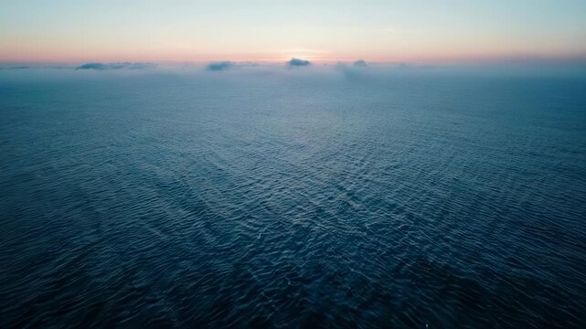 Aerial view of ocean at dawn, with cloud bank and subtle pink & blue sky gradients