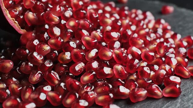 Vibrant Pomegranate Seeds Spill Across Dark Slate Surface, Showcasing Freshness and Detail