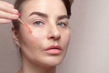 Fototapeta premium Caucasian woman applies serum from a pipette to her face.