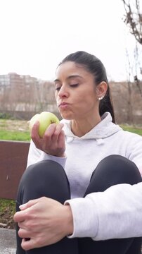 Athletic woman in sportswear taking a break and eating a fresh green apple in a park