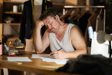 Middle-aged tailor struggling with paperwork in fashion studio