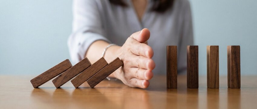 Businesswoman hand stopping the domino effect of wooden blocks for risk management concept