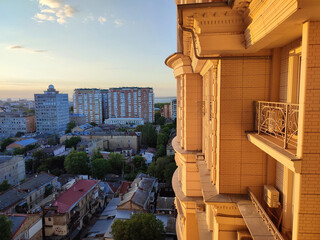 Cityscape with sea and blue sky on summer evening and sunlight illuminated white wall with windows of multi-story residential building. Old buildings, roofs, green trees. Front facade. Architecture