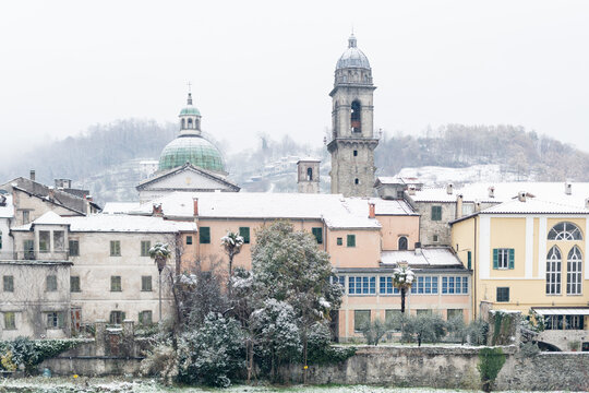 View of rooftops and buildings dusted with snow, while a dome and bell tower rise against a soft, wintry sky, Pontremoli, Tuscany, Italy.