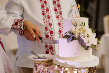 Bride and groom cutting wedding cake together in traditional Ukrainian embroidered attire at...