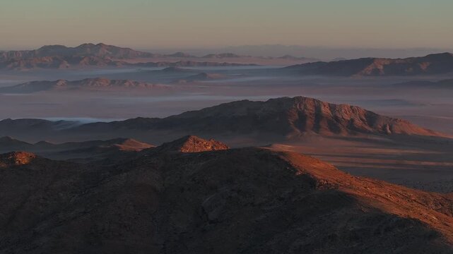 Dawn over Namib desert aerial view. Slow pan across desolate landscape. Mist rising between mountains over plains.