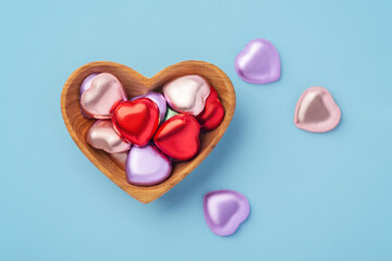 Chocolate hearts with colorful foil wrapped in heart wood bowl on blue background, Valentine's day celebration, top view