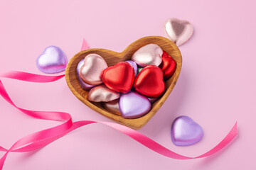 Valentine's day and love concept, Heart chocolate with colorful foil wrapped in heart wooden bowl with ribbon decorated on pink background