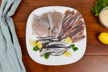Raw mixed fish on a white plate. Fillets of saithe and anchovies. Flat lay.