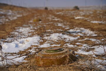 Naklejka premium An anti-personnel mine is lying on the ground among the soil and snow.