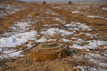Naklejka premium An anti-personnel mine is lying on the ground among the soil and snow.