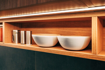 Modern kitchen open shelf with metallic spice shaker jars and white wooden bowls under warm LED...