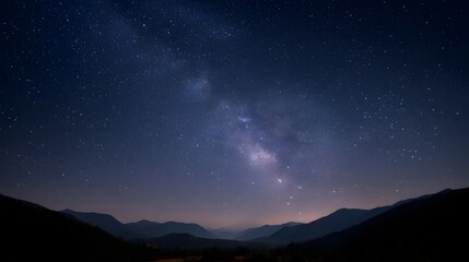Fototapeta premium The Milky Way galaxy arches across a deep blue night sky above silhouetted mountain ranges