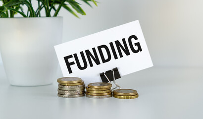 Text Funding and coins on white table and potted flower