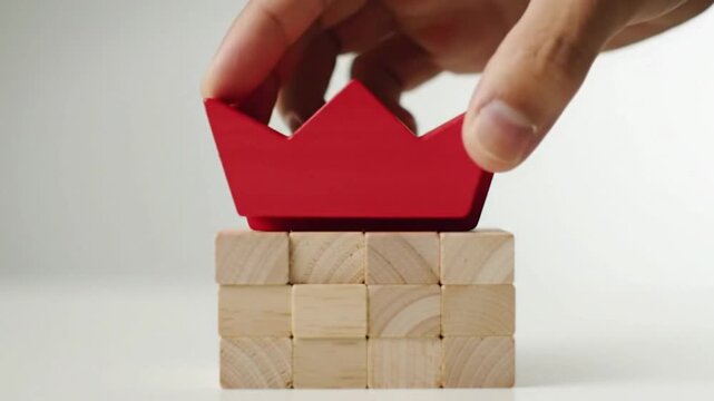 Leadership concept, close-up of hand placing a red boat-shaped block on top of a stack of neutral wooden blocks, symbolizing uniqueness, excellence, direction, and standout performance, clean min