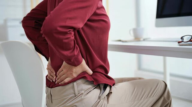 Female worker experiencing lower back pain while sitting at office desk. Concept of poor posture, sedentary lifestyle, and ergonomic discomfort.