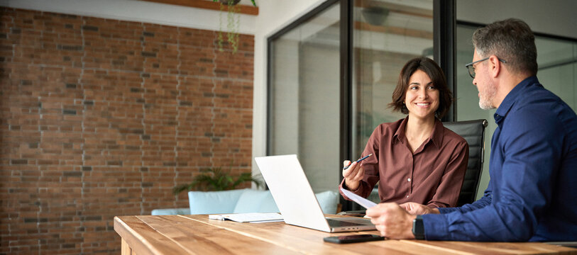 Two happy executives working on laptop discussing financial documents at meeting. Professionals team talking planning project at work. Attorney or bank manager consulting client investor in office.