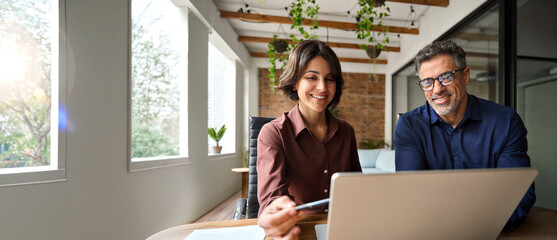 Two happy busy male and female business people working at desk using laptop computer in office....